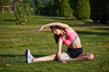 atletik kız güzel park çimenlere oturmuş germe egzersiz yaparak