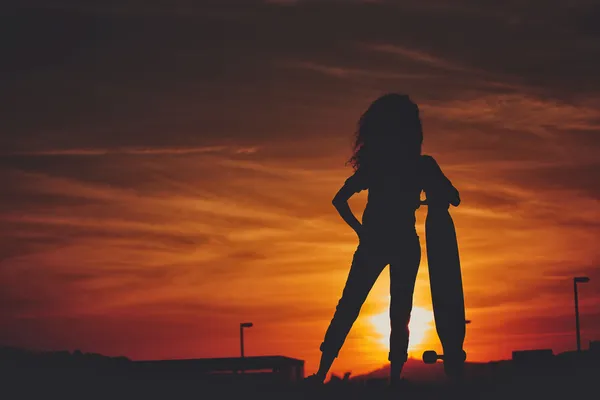 Silhouette of the beautiful girl with the longboard in the sunset — Stock Photo, Image