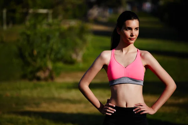 Schöne athletische Mädchen steht im grünen Park nach dem Joggen — Stockfoto