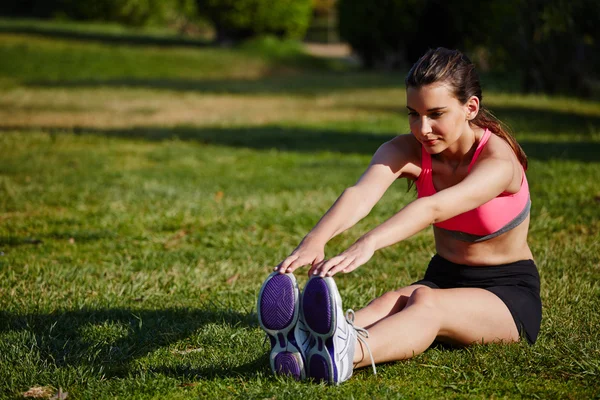 Athletic girl doing stretching exercise seated on the grass in the beautiful park — Stock Photo, Image