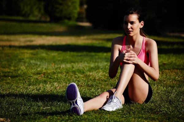 Athletic girl doing stretching exercise seated on the grass in the beautiful park — Stock Photo, Image