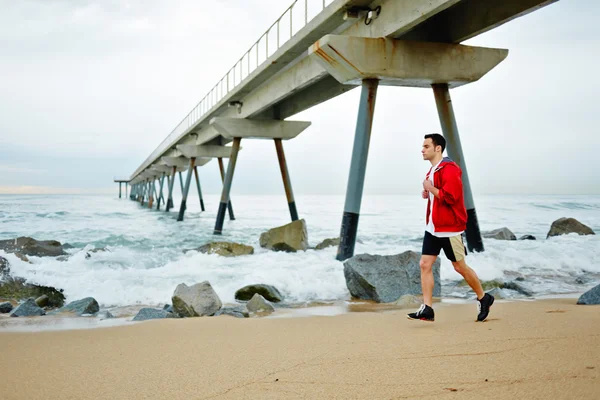 Jonge atleet in wit t-shirt loopt op het zand langs het strand genietend van de prachtige ochtendzee — Stockfoto