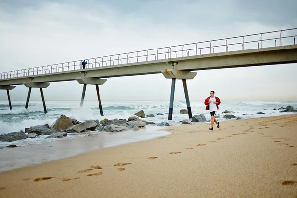 Junger Sportler im weißen T-Shirt läuft am Strand entlang und genießt das wunderschöne Morgenmeer — Stockfoto