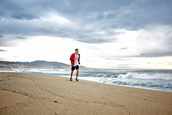 Jovem atleta homem em t-shirt branca corre na areia ao longo da praia apreciando o belo mar da manhã — Fotografia de Stock