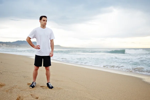 Young athlete man resting after morning jogging on the beach Stock Image