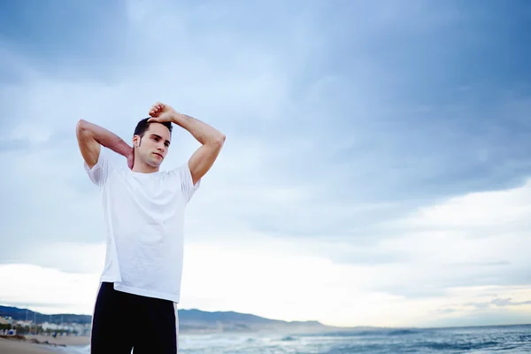 Tired after workout outdoors male runner stand on the beach with cloudy sky on background — Stock Photo, Image