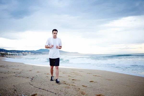 Young brunette man with towel on the shoulders walking on the sand — Stock Photo, Image