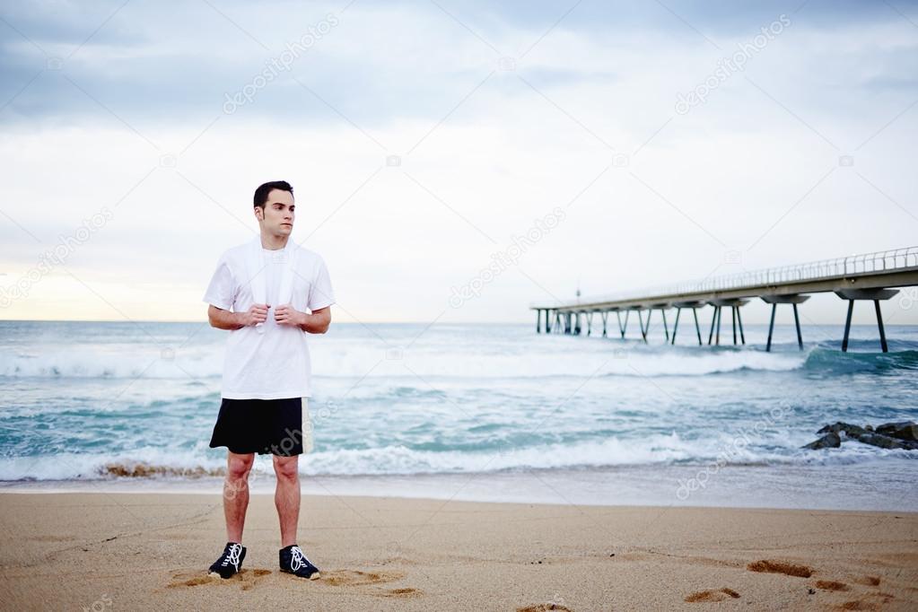 Beautiful young sportsman resting after run staying on the beach