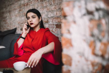 Renkli makyajlı hüsnükuruntulu bir kadın yemek molasında modern kafeteryada masa başında otururken akıllı telefondan iş planları hakkında konuşuyor.