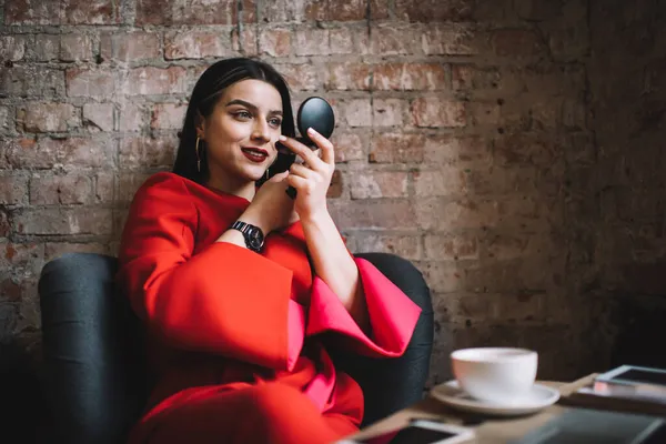 Şık kırmızı elbiseli genç, zarif esmer. Eski püskü tuğla duvarlı modern kafede bir fincan kahvenin tadını çıkardıktan sonra koyu kırmızı ruj sürüyor.