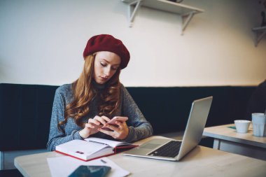 Modern dizüstü bilgisayar ve not defteriyle masada oturan ciddi kadın serbest yazar işten sonra boş zamanı olan sosyal ağları kontrol ediyor.