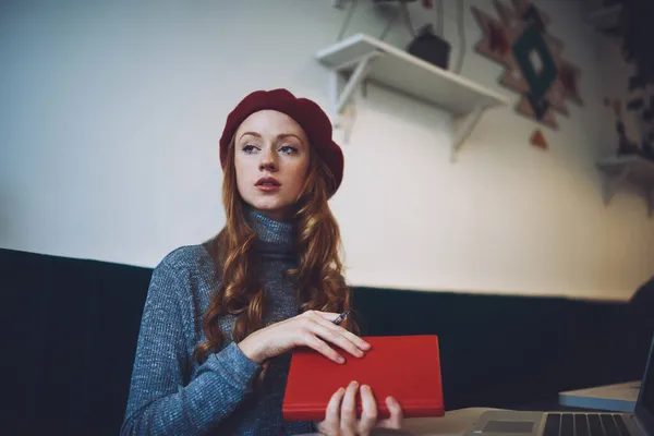 ベレー帽をかぶったカジュアルな服を着た若い女性の下からペンとメモ付きのテーブルに座って待っています — ストック写真