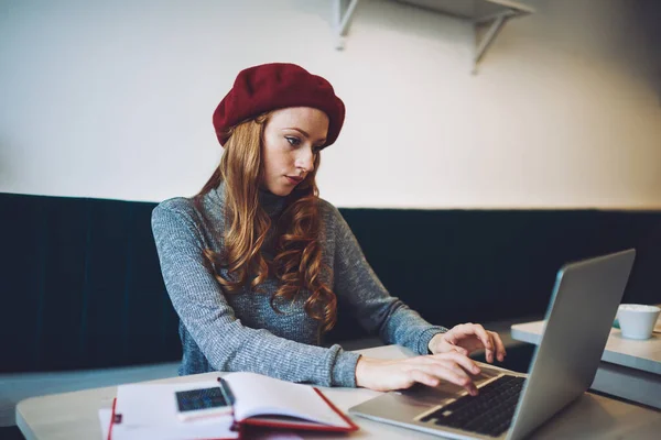 年轻的女自由职业者坐在桌旁 一边看着现代笔记本电脑的屏幕 一边寻找新项目的信息 一边在轻松的工作空间里工作 — 图库照片