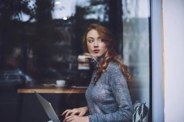 通过对穿着休闲装 有魅力的红头发女自由职业者的镜面观察 我们可以看到她们白天在咖啡店的笔记本电脑上打字时 眼睛都移开了 — 图库照片