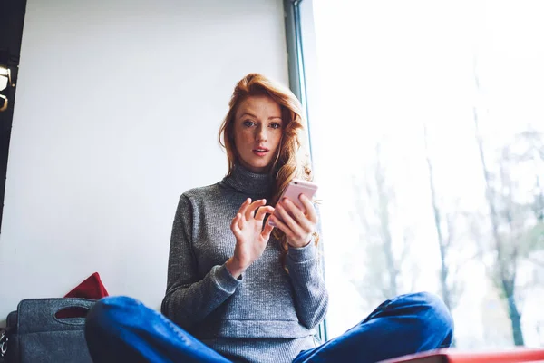 Låg Vinkel Allvarlig Kvinna Casual Kläder Tittar Kameran Sitter Fönsterbrädan — Stockfoto