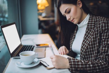 Ödev yapan genç bayan ciddi öğrencinin kafeteryada bir fincan kahve ve dizüstü bilgisayarla masada oturması.