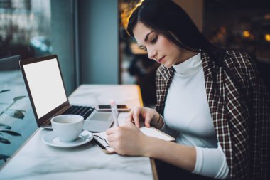 Kafeteryada elinde bir fincan kahve ve taşınabilir dizüstü bilgisayarla masa başında oturan ve gündüzleri gazetelerle uzaktan yakından ilgilenen bir serbest çalışan genç kadın.