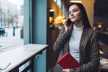 Kareli ceketli neşeli genç bir bayan ve kırmızı defterli beyaz bir bluz kafede cep telefonuyla konuşurken gözlerini kaçırıyor.