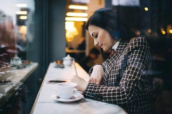 女子大生がコーヒーを飲みながらテーブルに座り 大学の課題に取り組みながらメモを取る様子 — ストック写真