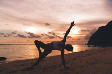 Anonim kadın silueti, akşam yoga eğitiminde sakin deniz kenarında yan tahta pozisyonu alıyor.