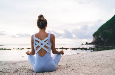 Spor kıyafetli, plajda Lotus pozu vermiş, Bali sahilinde meditasyon yapan kimliği belirsiz bir kadın.
