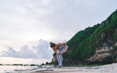 Yaz mevsiminde deniz kenarındaki kayalık sahilde yoga yapan genç bir dişinin boyunun altında.