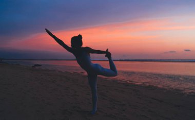 Siluet görünümlü zayıf kadın yoga egzersizleri sırasında yoga yapıyor, sakin kadın jimnastik yapıyor gün batımında sportif meditasyondan keyif alıyor.