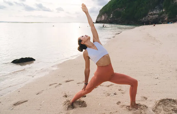 มมองด านข างของผ ยบสงบในช ดแอคท Vipita Virabhadrasana Asana ในขณะท กโยคะบนชายหาดทรายใกล — ภาพถ่ายสต็อก