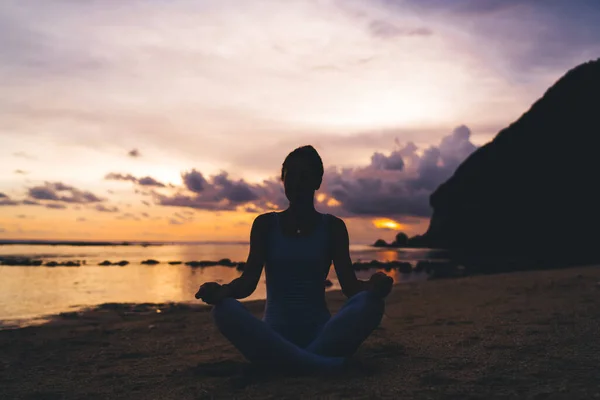 バリの海岸にある蓮の花のポーズで砂浜に座って 日没の間に瞑想を練習するスポーツウェアの認識できない女性の完全な体 — ストック写真