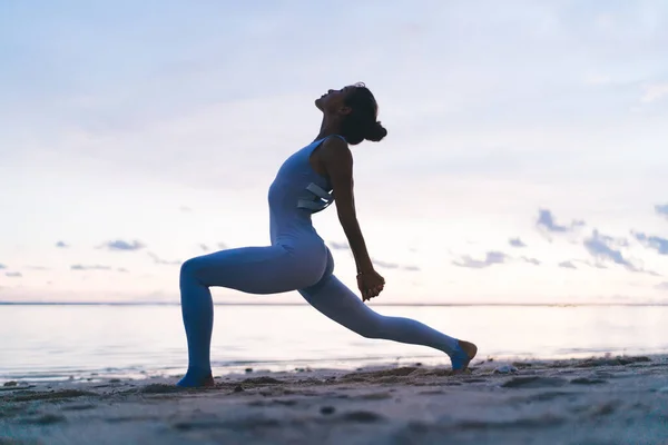 在平静的海面上练习瑜伽时 侧看身穿活动服的柔韧女子站在新月形隆起时的姿势 双手交叉在背后伸展 — 图库照片