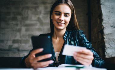 Neşeli bayan, beyaz kartvizitten modern cep telefonu teknolojisinde arama yapmak için kontağı kontrol ediyor. Kafkasyalı öğrenci cep telefonuyla arama yapmak için bilgi içeren kağıt üzerinde mesaj okuyor.
