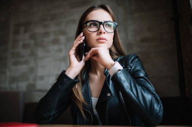 Mobil teknolojiyi danışmanlık için kullanarak göz koruması sağlayan, şık gözlüklü düşünceli hippi kız, telefon görüşmeleri sırasında alınan bilgiler üzerine kafa yoran beyaz kadın.