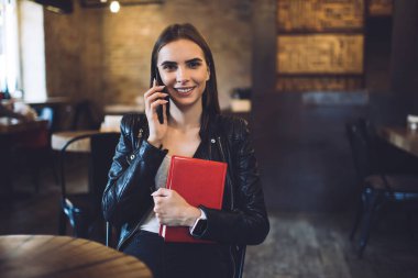 Eğitim notlu komik hipster kızın yarım boy portresi kameraya gülümserken aynı zamanda edebiyat entrikalarını tartışmak için en iyi arkadaşına sesleniyor mutlu öğrenci internet bağlantısını telefon etmek için kullanıyor.