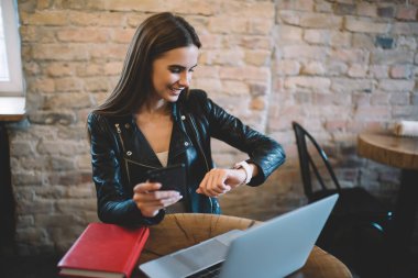 Kafkasyalı mutlu yönetici elinde cep telefonu cihazını tutuyor ve giyilebilir akıllı kaseti kontrol ediyor, modern teknolojileri kullanarak, kahve dükkanında uzaktan kumanda ederken gülümseyen kadın serbest çalışıyor.