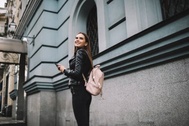 Mutlu kadın milenyumu, turistik sırt çantasıyla şehir binasının yakınında cep telefonu kullanarak gülümseyen, gezici cihazlı neşeli hippi kız bahar tatillerinde gezintiye çıkıyor.