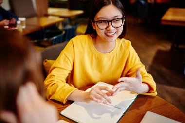Kafeteryada defter ile masada otururken günlük kıyafetlerle sohbet eden çok ırklı genç bayan arkadaşların yüksek açısı.