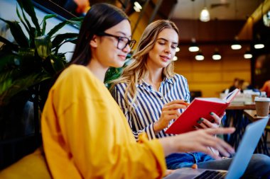 Modern kafede rahat bir kanepede otururken dizüstü bilgisayar ve not defteriyle çalışan modaya uygun giyinmiş çeşitli bayan öğrencilere odaklandık.