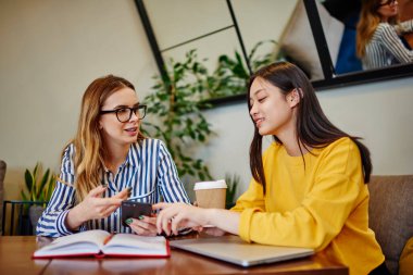 Not defteri ve dizüstü bilgisayarla masada oturan ve kafedeki projenin detaylarını tartışırken akıllı telefonları karıştıran pozitif çok ırklı meslektaşlar