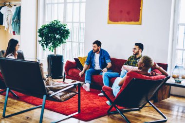 Çeşitli giyinmiş hippi erkekler hafta sonu ev içi hobileri hakkında konuşuyorlar, en iyi arkadaşlar modern apartmanda sosyalleşiyorlar rahat oturma odasında iletişim kuruyorlar.