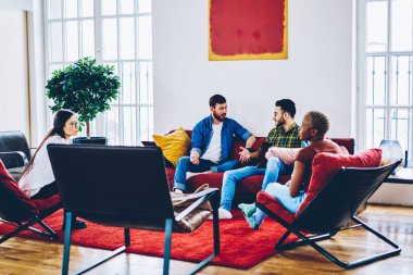 Yaratıcı erkek ve bayan meslektaşlardan oluşan genç bir grup modern iç mimari fikirleri kırmızı mobilyalarla tartışıyor, genç hippiler misafir toplantısı sırasında konuşmak için boş vakitlerini harcıyorlar.