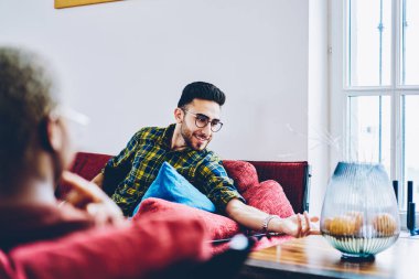 Moda gözlüklü mutlu Ortadoğu erkeği göz düzeltmesi yapıyor. Kesilmiş en iyi arkadaşıyla eğleniyor. Gözlüklü genç hippi evde dinlenmeyi tartışıyor.