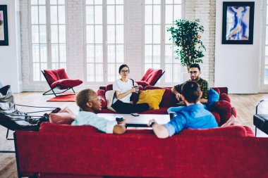 Çeşitli hipster grupları hafta sonu boş zamanlarını evdeki oturma odasında sohbet ederek geçiriyorlar. Boş zamanlarında servis bardakları olan genç erkek ve kadın arkadaşlar kanepenin üzerinde iletişim kuruyorlar.