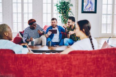 Heyecanlı hippi erkekler gündelik giyinip zaferi kutlarken dijital tabletten canlı yayın izliyorlar ve modern apartman dairesinde genç kadınlar sohbet ederken 4G internet kullanıyorlar.