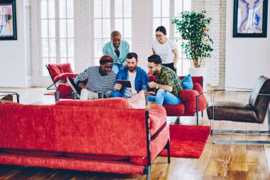 Genç hipster 'lar modern dairede boş zamanlarında internet haberlerini kontrol etmek için dokunmatik ped kullanıyorlar. Erkekler ve kadınlar rahat kanepede dinleniyorlar. Yurttaki mesaj ağı içeriği hakkında konuşuyorlar.