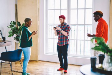 Modern akıllı telefonlarda bluetooth 'a bağlı online oyun oynayan çeşitli erkek ve kadın arkadaşlar. Dairede web tarayıcı olarak cep telefonu cihazları kullanan mutlu hipsterler.