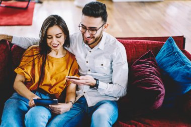Aşık komik bir çift, hafta sonu harcamaları sırasında cep telefonu ve dokunmatik ağlar kullanıyor, dijital tablette 4G 'ye bağlanan mutlu çok ırklı hipsterler ve sohbet için cep telefonu kullanıyor.