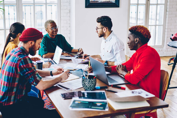 Skilled hipster guys communicate and briefing at table desktop with modern netbook device for projecting, young male and female colleagues collaborating during brainstorming meeting on freelance