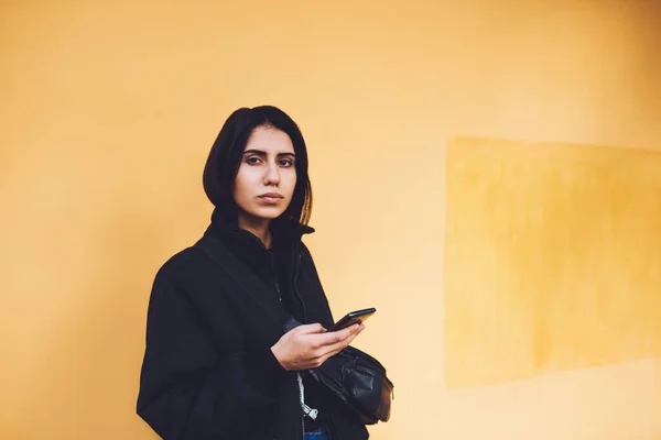 Серьёзные Женщины Черной Одежде Смотрят Камеру Стоя Оранжевой Стены Используют — стоковое фото