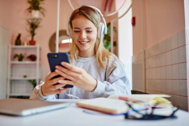 Elektronik kulaklıklı Mutlu Kafkasyalı blogcu, ses yalıtımı için modern akıllı telefon cihazından müzik yayını seçiyor, kulaklıklı neşeli hippi kız, pozitif ses kayıtlarını dinliyor.