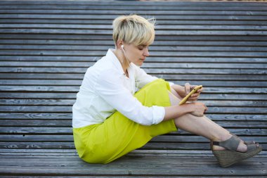 Modern akıllı telefon teknolojisinde müzik podcast 'i seçen elektronik kulaklıklı modaya uygun giyinmiş yeniyetme kızın yan görüntüsü, milenyum kadın blogcusu mobil uygulama üzerinden ses kaydı aldı